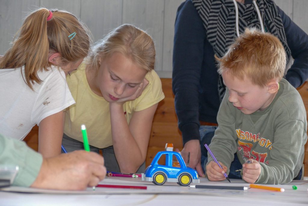 Kinderen tekenen op een groot vel papier op een tafel tijdens de Kinderkerk.